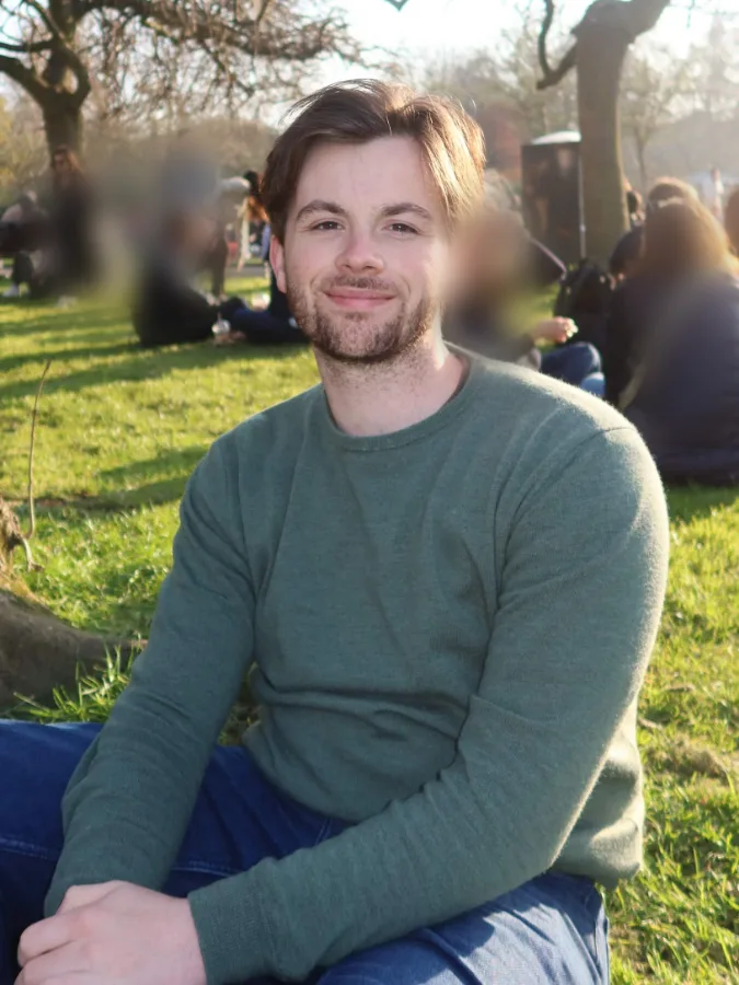 Sébastien, souriant, assis dans l'herbe d'un parc ensoleillé
